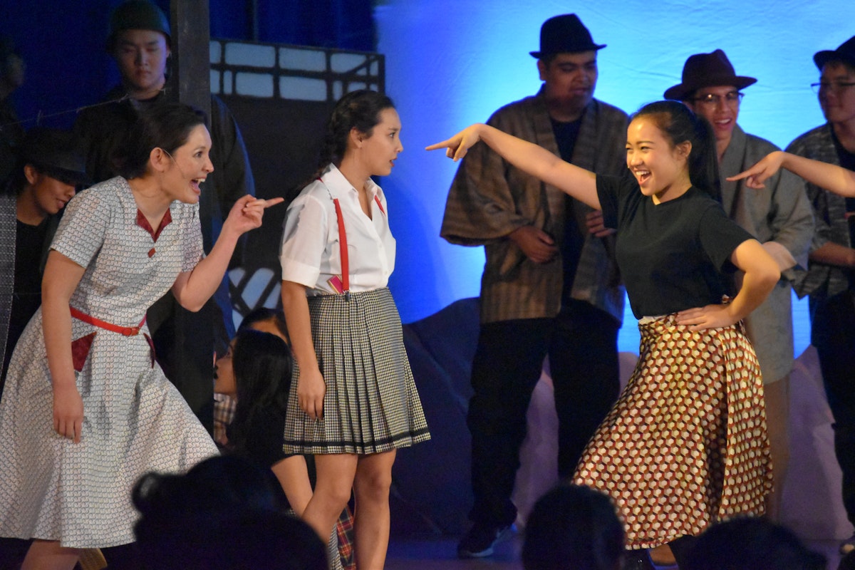 Teenagers smiling and gesturing expressively on stage in costume.
