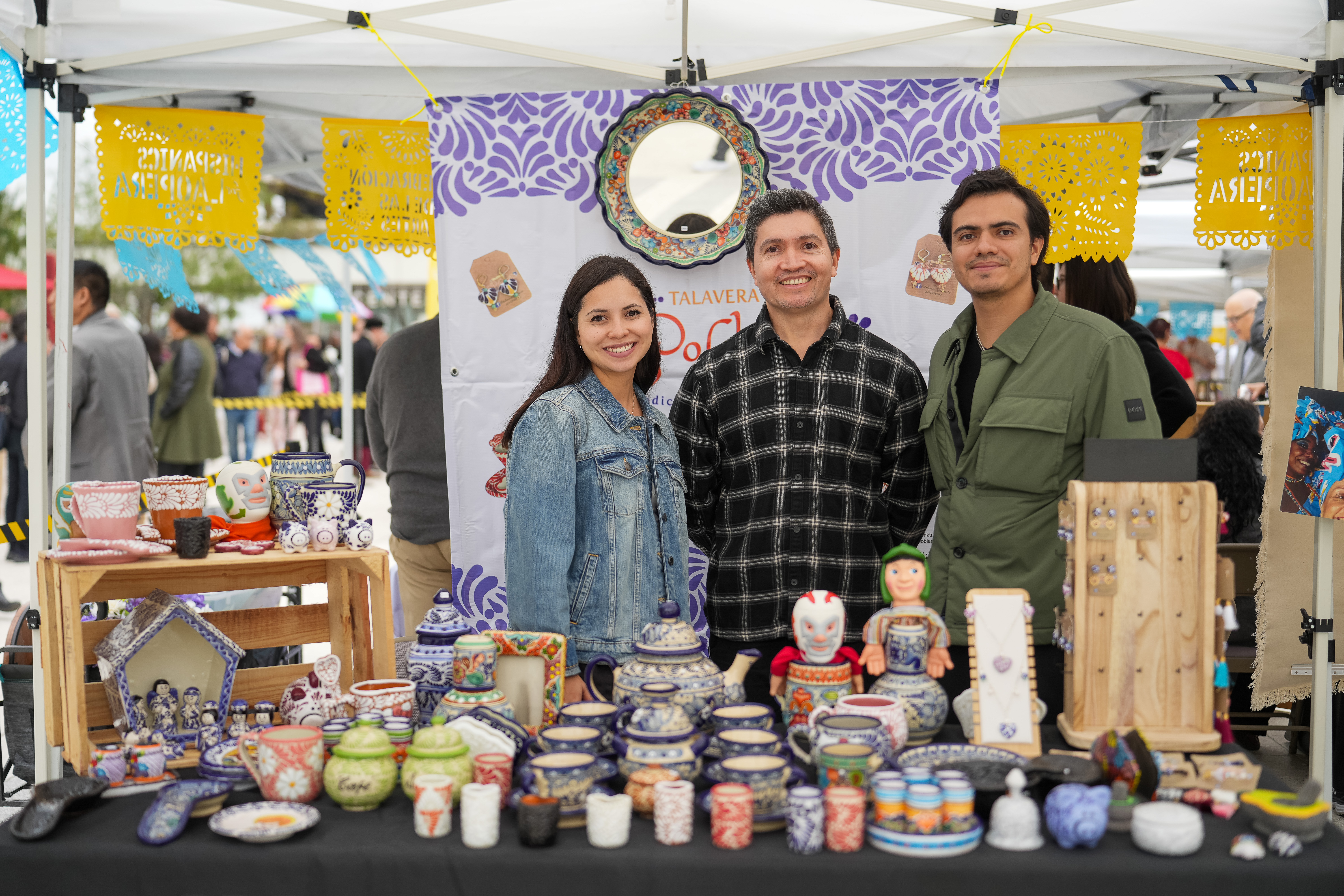 Pottery business owners posing in their colorful booth at the Celebración de las Artes