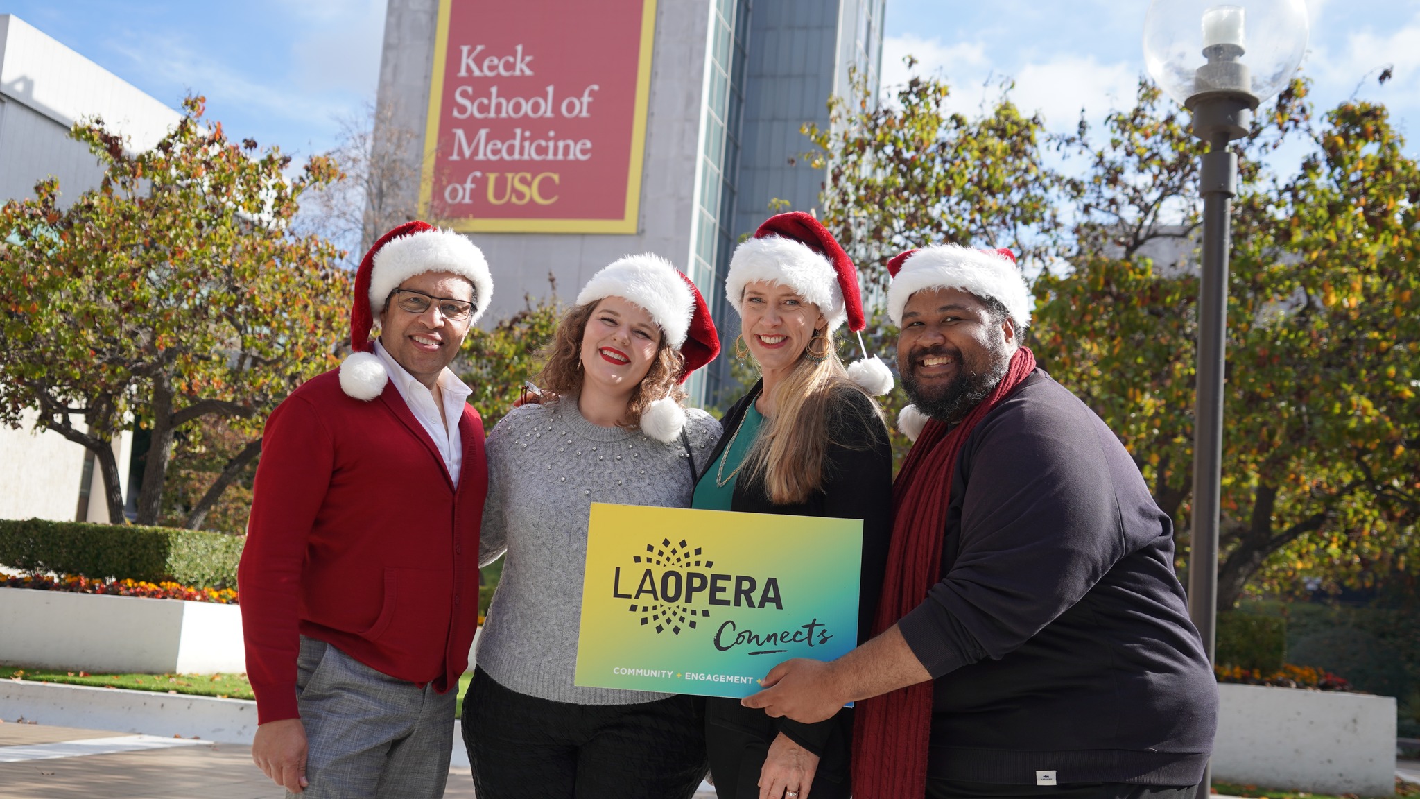 LA Opera Carolers posing in Santa Hats in front of USC Keck School of Medicine